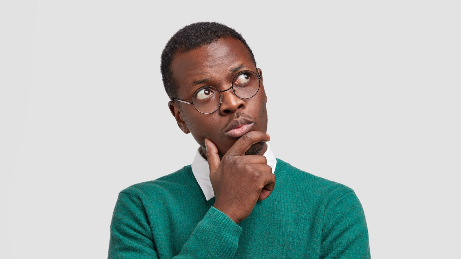 A man in glasses and a green sweater looks up thoughtfully with his hand on his chin. This visual can represent the decision-making process around implementing call recording for compliance or evaluating Microsoft Teams compliance recording solutions.