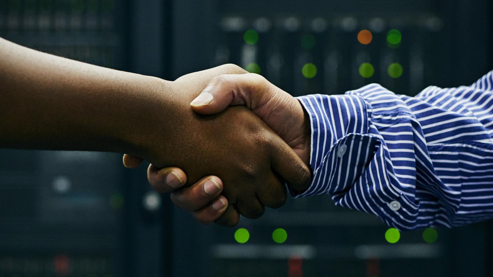 Two hands shaking in front of server lights, representing how MSPs can build more partnerships with TeamMate's offering.