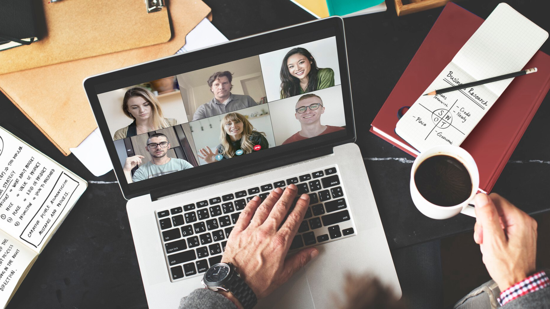 A laptop screen displays a virtual meeting with six participants, while a person types and holds a coffee mug at a desk. This image represents Teams call recording and cloud call recording for collaborative remote meetings and compliance tracking.
