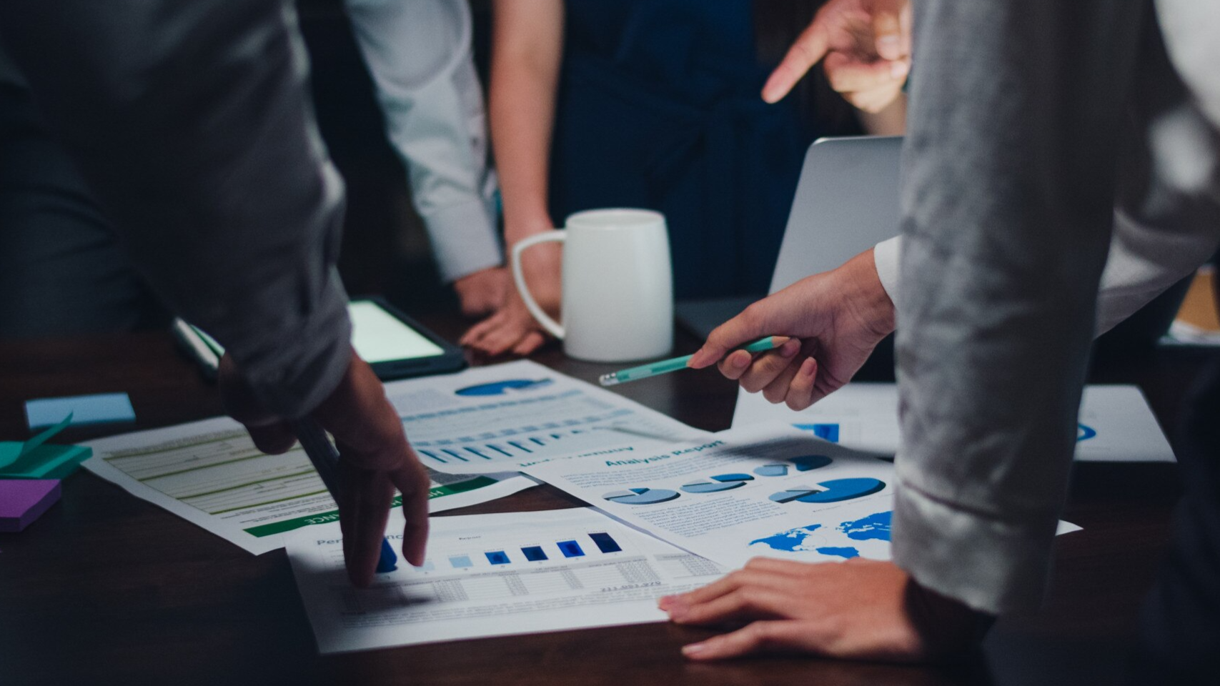 Close-up of a group of professionals gathered around a table reviewing printed charts and graphs, possibly during a discussion about Microsoft Teams phone call recording performance metrics or analytics for recording Teams calls.